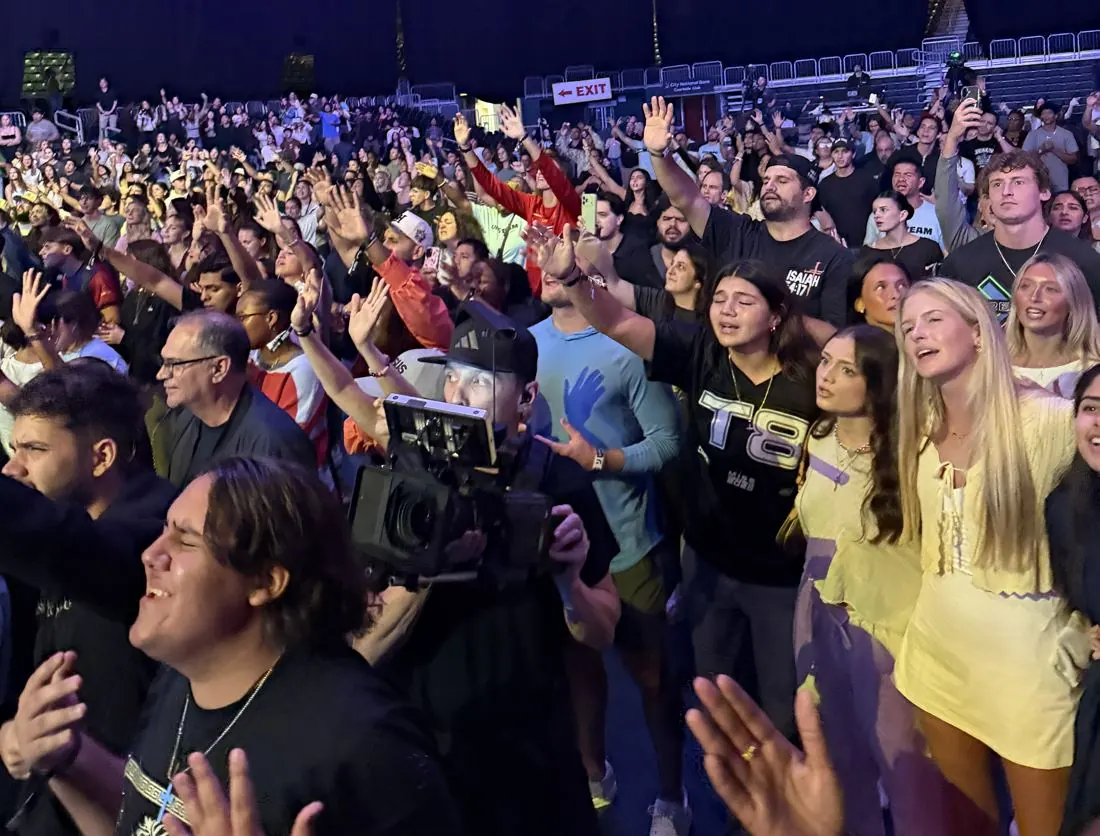 Packed arena crowd with a camera operator filming in the middle of the audience