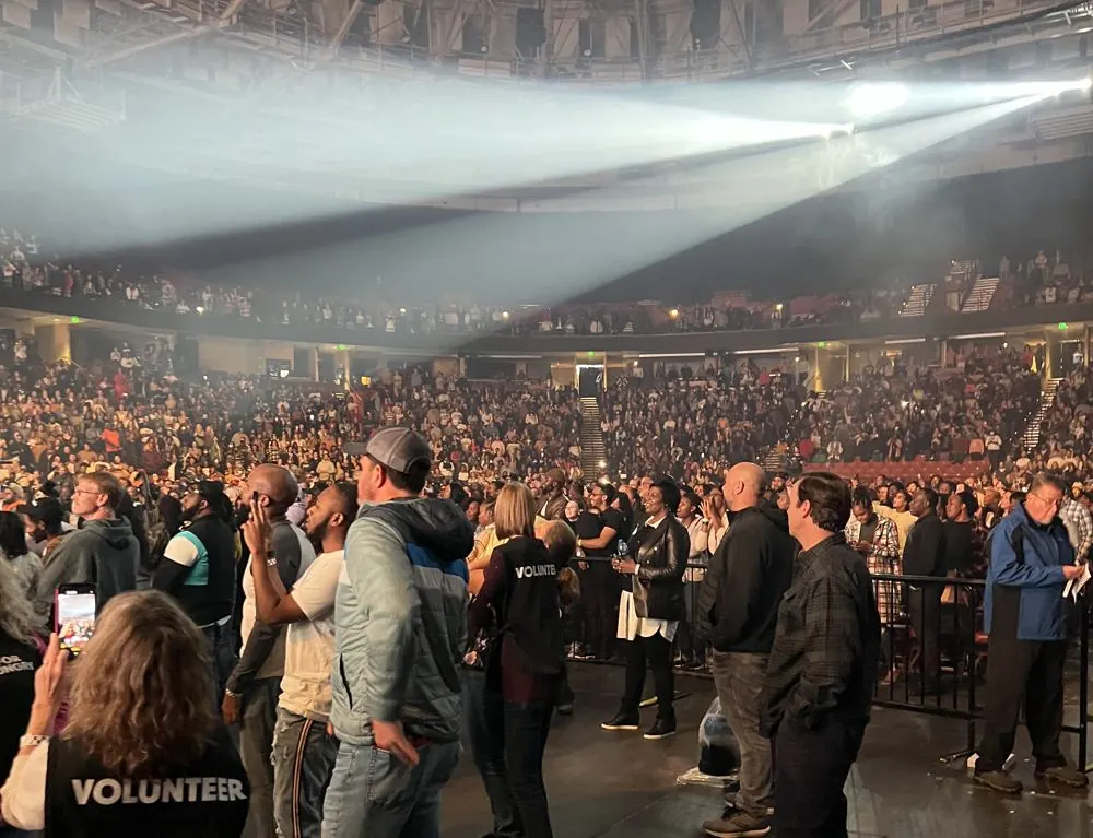 Packed arena with stage lights sweeping over the crowd