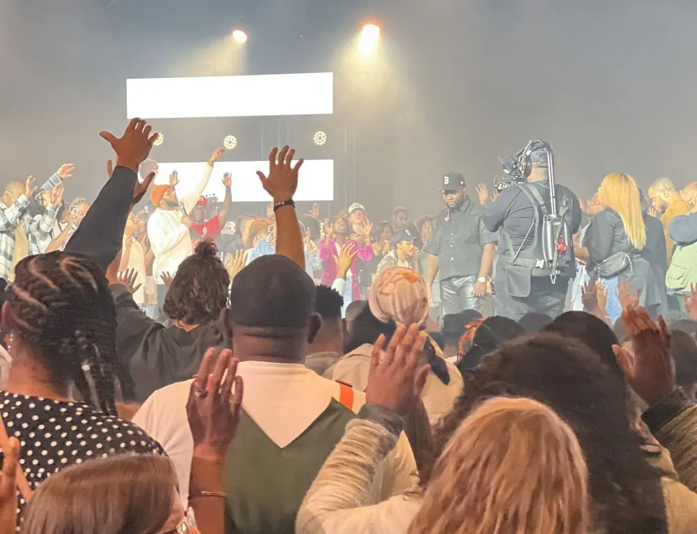 Crowd with hands raised in front of a stage while a camera operator films